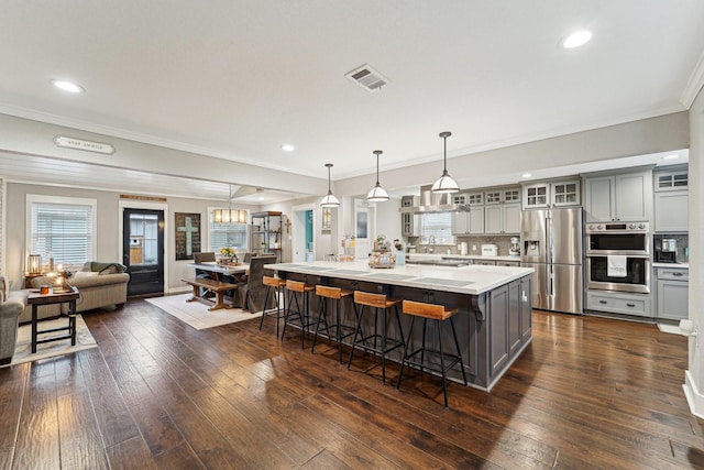 kitchen with gray cabinetry, appliances with stainless steel finishes, decorative light fixtures, and a large island with sink