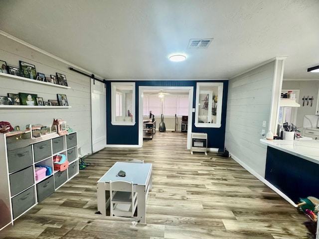 rec room featuring heating unit, hardwood / wood-style floors, crown molding, and a barn door