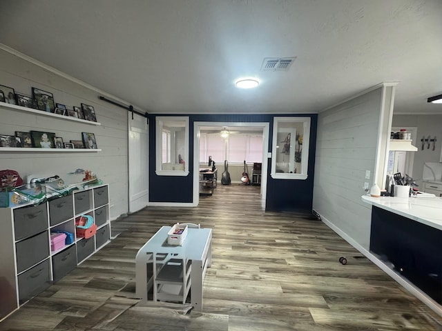 interior space with crown molding, dark wood-type flooring, a barn door, and wood walls