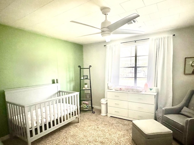 bedroom with light colored carpet, a nursery area, and ceiling fan