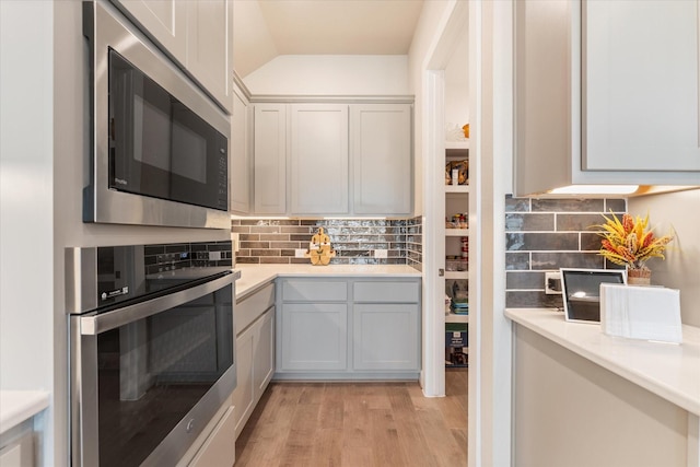 kitchen featuring backsplash, built in microwave, vaulted ceiling, oven, and light wood-type flooring