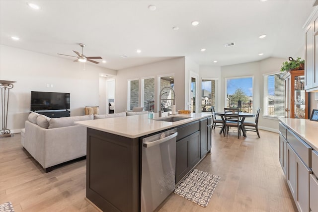 kitchen with sink, a kitchen island with sink, vaulted ceiling, stainless steel dishwasher, and light wood-type flooring