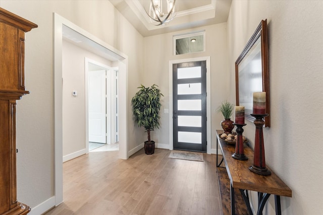 foyer with a raised ceiling, light hardwood / wood-style floors, and a notable chandelier