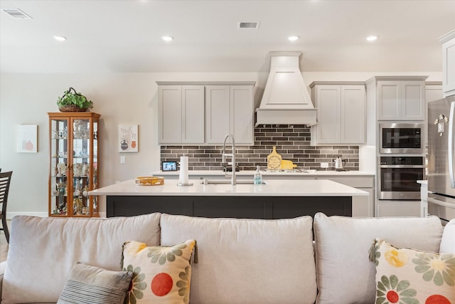 kitchen with appliances with stainless steel finishes, tasteful backsplash, an island with sink, sink, and custom exhaust hood