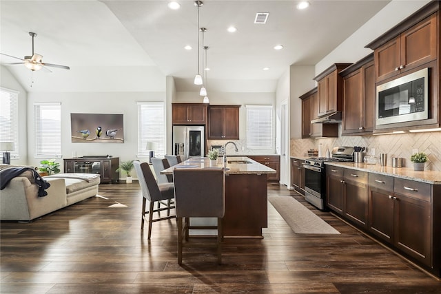 kitchen with appliances with stainless steel finishes, sink, a center island with sink, and light stone counters