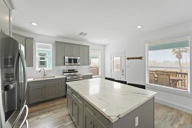 kitchen with sink, light hardwood / wood-style flooring, stainless steel appliances, a center island, and light stone countertops