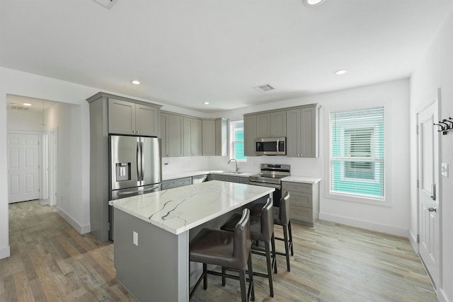 kitchen with a kitchen island, appliances with stainless steel finishes, wood-type flooring, a breakfast bar area, and light stone countertops