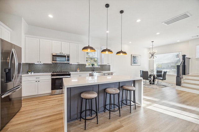 kitchen with stainless steel appliances, white cabinetry, and pendant lighting