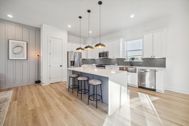 kitchen featuring sink, white cabinetry, hanging light fixtures, a kitchen island, and stainless steel appliances