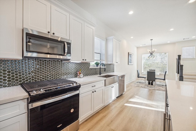 kitchen featuring sink, light hardwood / wood-style flooring, appliances with stainless steel finishes, pendant lighting, and white cabinets