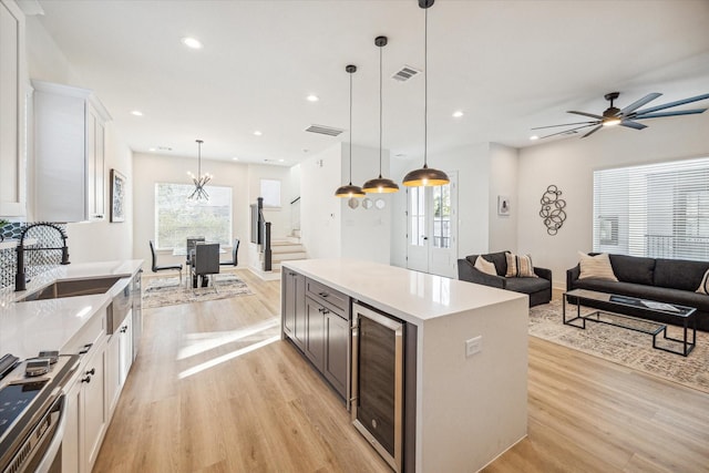 kitchen with wine cooler, hanging light fixtures, white cabinetry, and sink