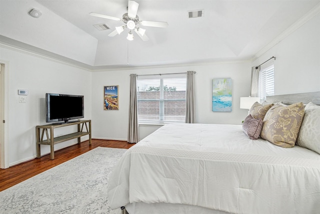 bedroom with lofted ceiling, hardwood / wood-style flooring, ornamental molding, ceiling fan, and a raised ceiling