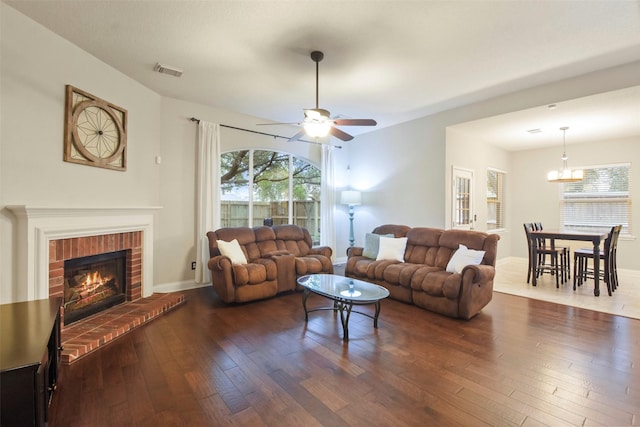 living room featuring plenty of natural light, dark hardwood / wood-style floors, ceiling fan with notable chandelier, and a brick fireplace