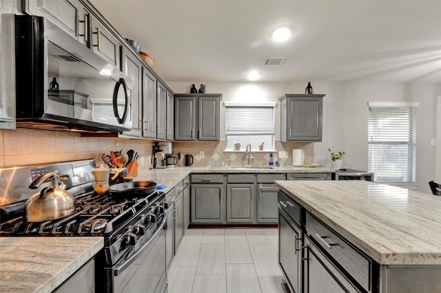 kitchen featuring appliances with stainless steel finishes, sink, gray cabinetry, decorative backsplash, and light stone countertops