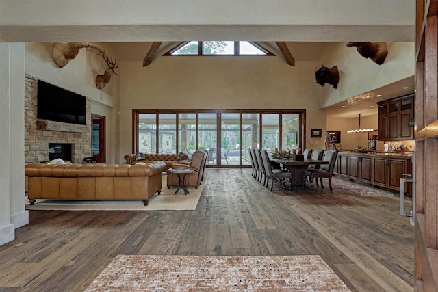 living room featuring beam ceiling, dark hardwood / wood-style flooring, a stone fireplace, and a high ceiling