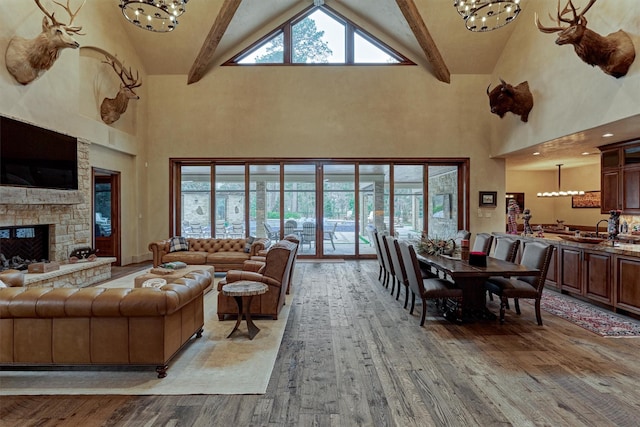 living room with an inviting chandelier, high vaulted ceiling, beamed ceiling, a fireplace, and light hardwood / wood-style floors