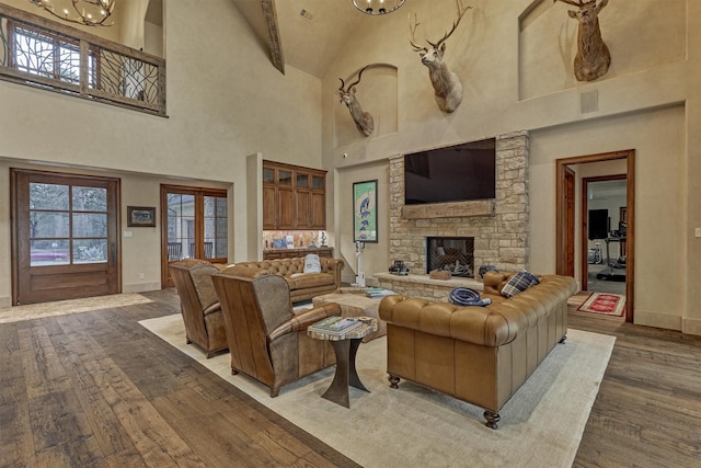 living room featuring a fireplace, a towering ceiling, wood-type flooring, and a chandelier