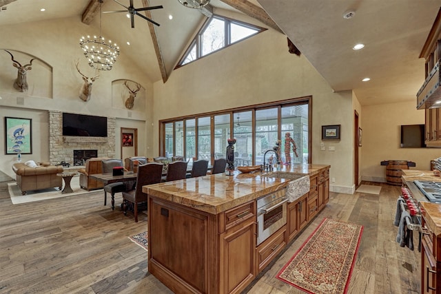 kitchen with sink, hardwood / wood-style floors, beam ceiling, a center island with sink, and a stone fireplace