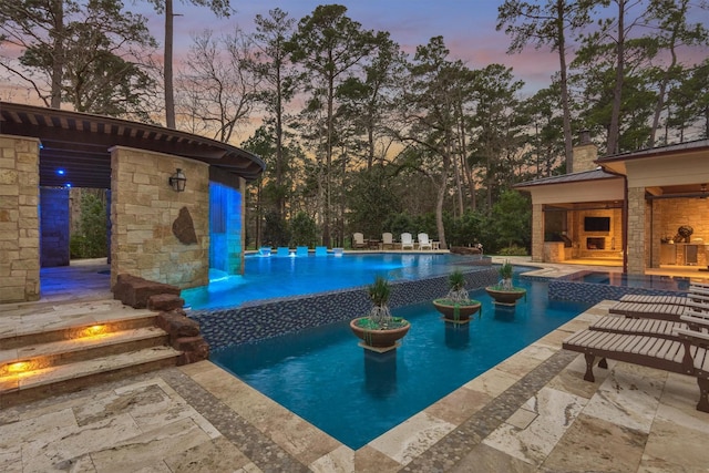 pool at dusk featuring a patio and an outdoor fireplace