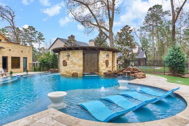 view of pool with pool water feature, a fireplace, a patio area, and an outbuilding