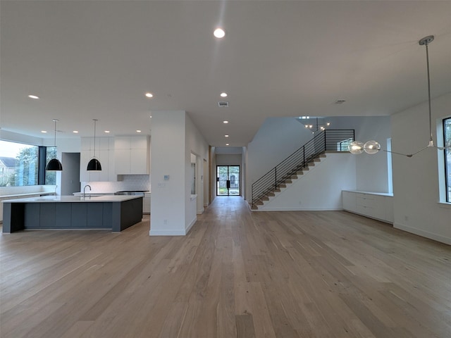 kitchen with sink, white cabinetry, hanging light fixtures, a center island with sink, and light hardwood / wood-style flooring