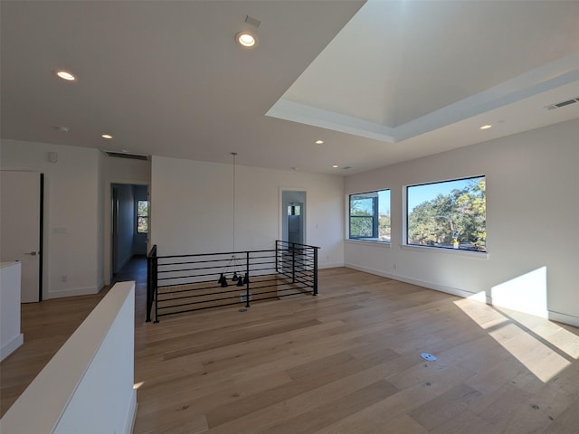 empty room featuring a tray ceiling and light hardwood / wood-style flooring