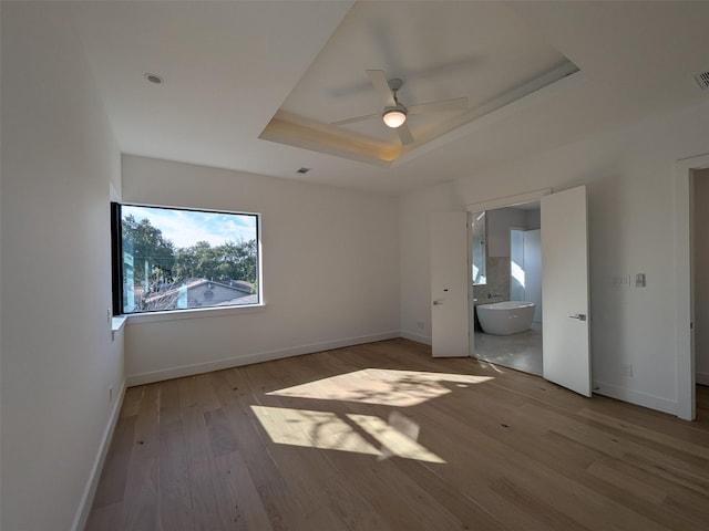 unfurnished bedroom with a raised ceiling, ceiling fan, connected bathroom, and light hardwood / wood-style floors