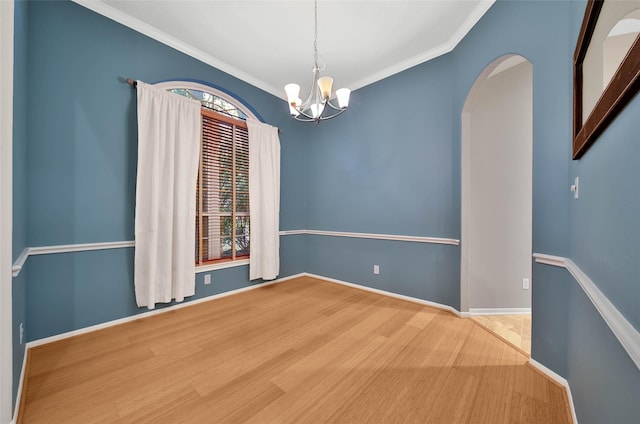 spare room featuring crown molding, wood-type flooring, and an inviting chandelier