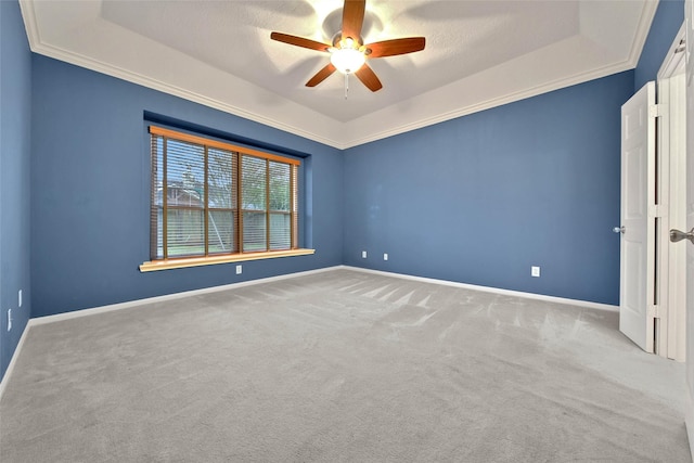 carpeted spare room with a raised ceiling, ornamental molding, and ceiling fan