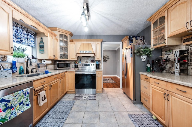 kitchen with stainless steel appliances, sink, light stone counters, and custom range hood