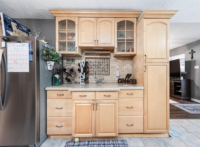 kitchen with stainless steel fridge, backsplash, light tile patterned floors, light brown cabinets, and a textured ceiling