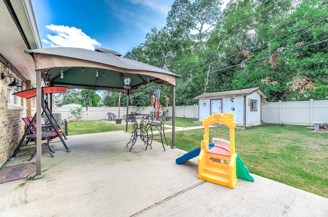 view of playground featuring a shed, a gazebo, a lawn, and a patio area