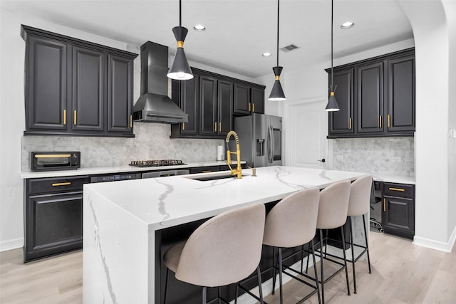 kitchen featuring pendant lighting, sink, range hood, stainless steel appliances, and an island with sink