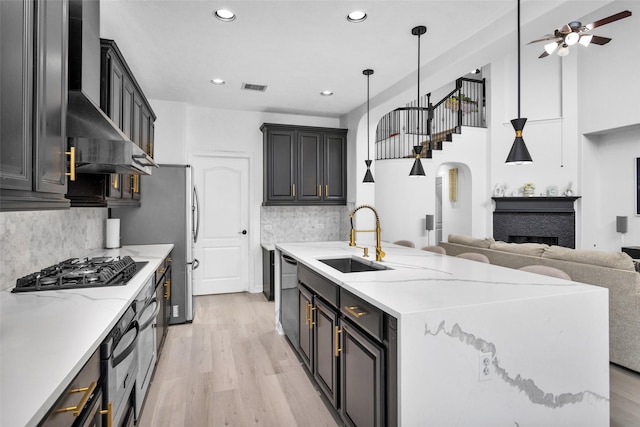 kitchen featuring sink, light hardwood / wood-style flooring, stainless steel appliances, decorative light fixtures, and wall chimney exhaust hood