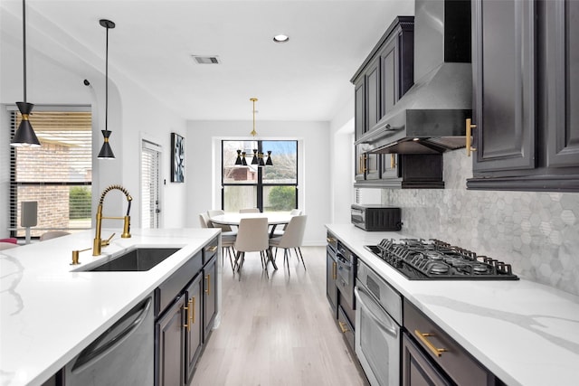 kitchen featuring sink, hanging light fixtures, stainless steel appliances, light stone countertops, and wall chimney range hood