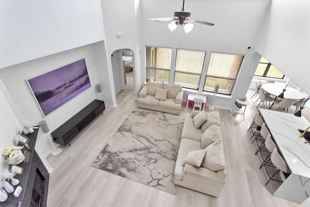 living room featuring ceiling fan, a towering ceiling, and light hardwood / wood-style floors