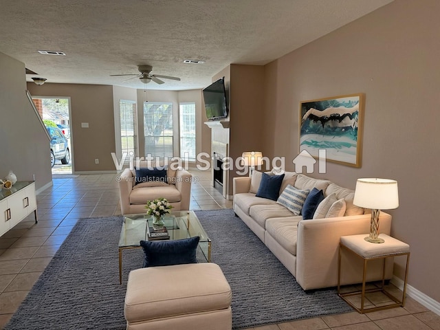 living room featuring a textured ceiling, a fireplace, visible vents, baseboards, and tile patterned floors