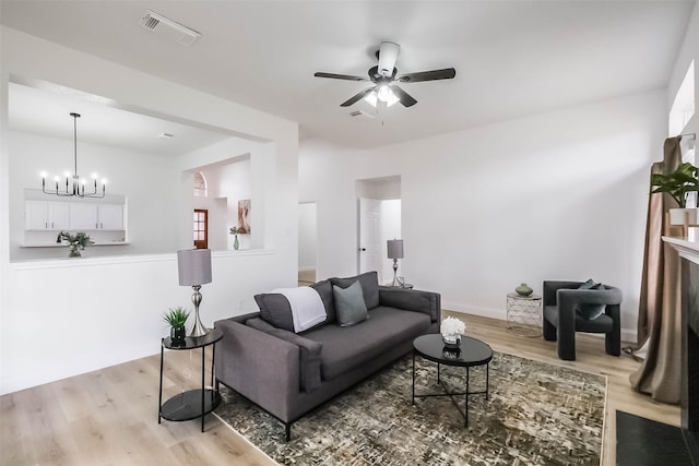 living room with ceiling fan with notable chandelier and light hardwood / wood-style floors