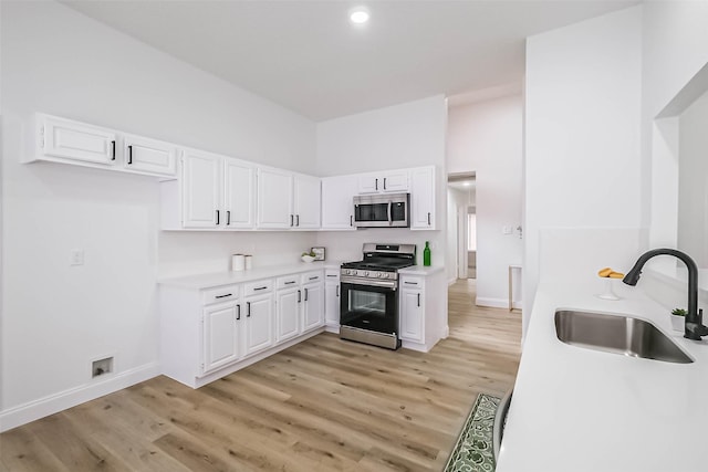 kitchen with appliances with stainless steel finishes, sink, light hardwood / wood-style flooring, and white cabinets