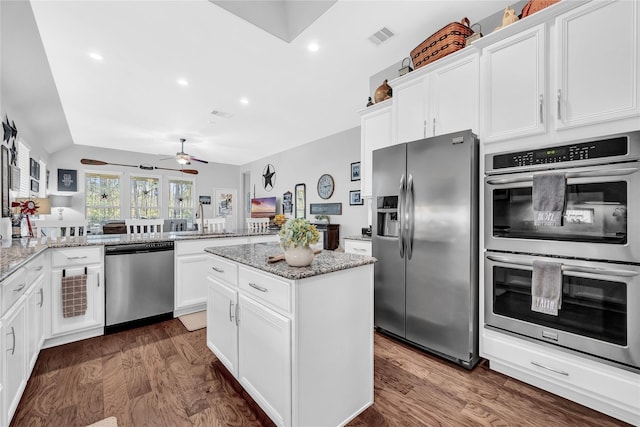 kitchen with light stone counters, appliances with stainless steel finishes, dark hardwood / wood-style flooring, kitchen peninsula, and white cabinets