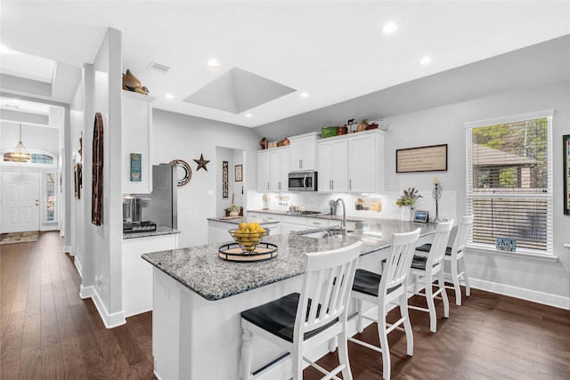 kitchen with a kitchen breakfast bar, light stone countertops, white cabinets, dark hardwood / wood-style flooring, and kitchen peninsula