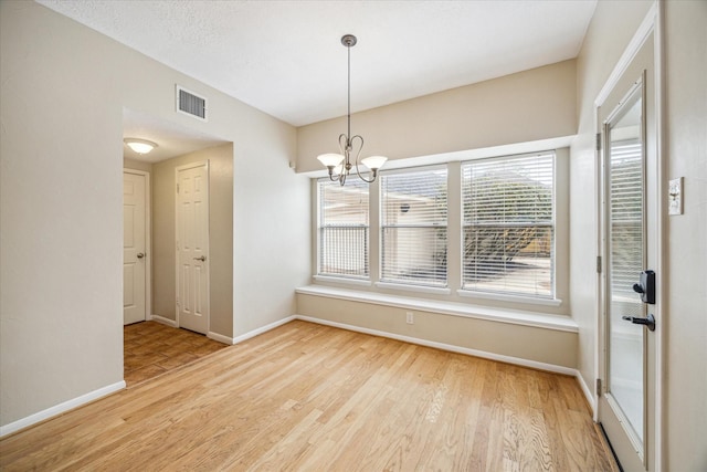 unfurnished dining area with baseboards, visible vents, a chandelier, and wood finished floors