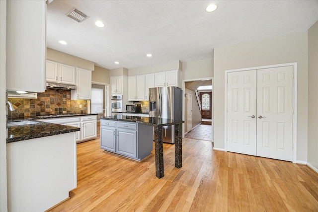 kitchen with under cabinet range hood, stainless steel appliances, a sink, visible vents, and white cabinets