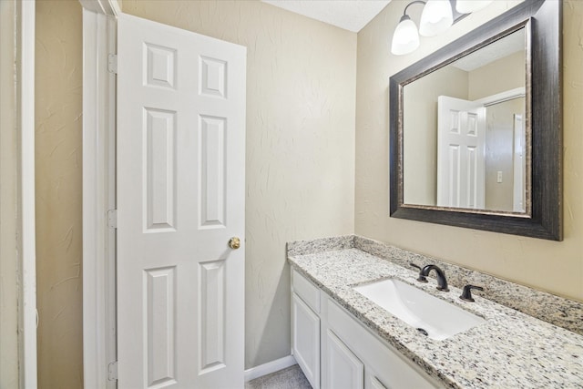 bathroom with a textured wall, vanity, and baseboards