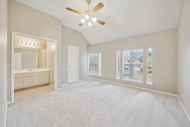 unfurnished bedroom featuring a ceiling fan, light carpet, vaulted ceiling, ensuite bath, and baseboards