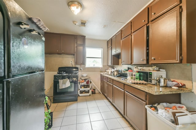 kitchen with light tile patterned flooring, light stone counters, black appliances, a textured ceiling, and backsplash