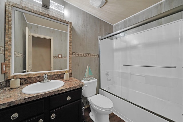 full bathroom with bath / shower combo with glass door, tile walls, ornamental molding, vanity, and toilet