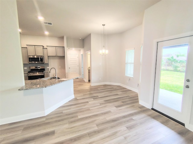 kitchen with pendant lighting, sink, light hardwood / wood-style flooring, stainless steel appliances, and light stone counters