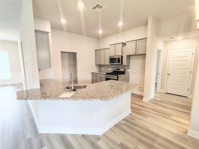 kitchen with sink, gray cabinetry, kitchen peninsula, stainless steel appliances, and light stone countertops