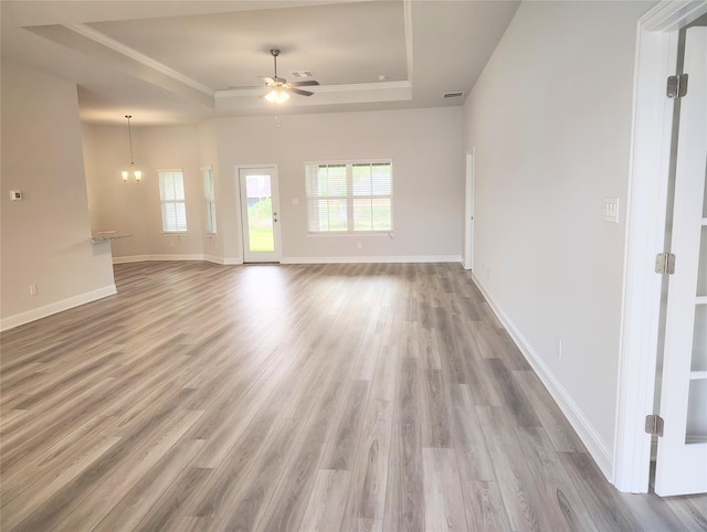 spare room with ceiling fan with notable chandelier, a healthy amount of sunlight, a raised ceiling, and hardwood / wood-style floors